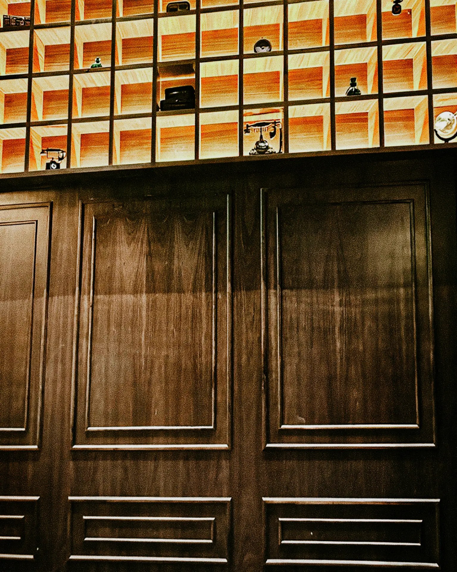 Backlit card-catalog cubbies of vintage curios above dark walnut paneling at Archive Sacramento